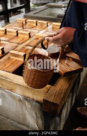 Nozawa onsen, Nagano, Japon, 2021-26-09 , une femme verse un panier d'oeufs à l'intérieur de l'eau chaude pour cuisiner à Nozawaonsen Banque D'Images