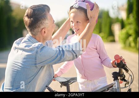 Papa mettant sa fille sur un casque de vélo Banque D'Images