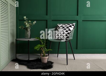 Chaise moderne et vase en verre avec eucalyptus sur la table à l'intérieur de la salle de séjour verte Banque D'Images