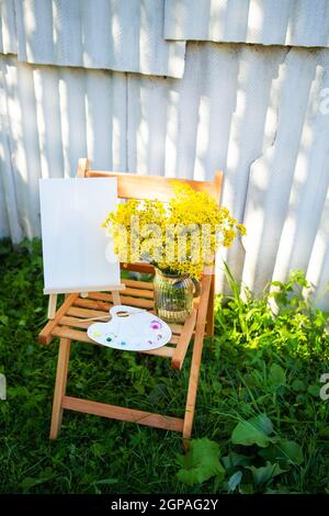 Une palette de peintures multicolores aquarelle se dresse sur une chaise en bois et un bouquet de fleurs jaunes, un passe-temps créatif. Jour ensoleillé Banque D'Images