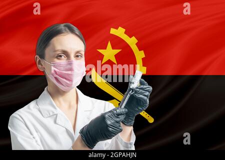 La jeune fille prépare la vaccination contre le fond du drapeau de l'Angola. Concept de vaccination Angola. Banque D'Images