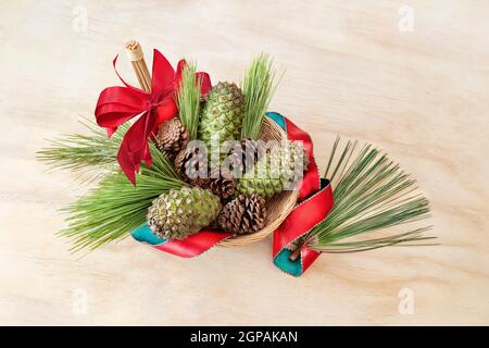Cornets de pin, verts et bruns, dans un panier en osier sur fond de bois clair. Ribon rouge et arc. Copier l'espace. Banque D'Images
