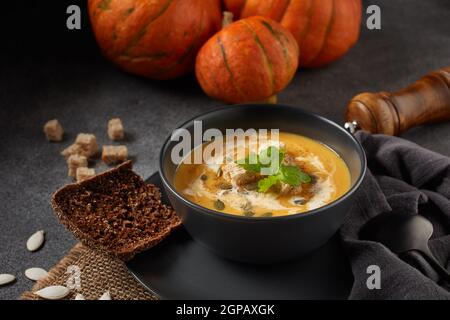 Soupe à la crème de potiron aux graines de potiron et cubes de pain séchés. Menu Lenten. Nourriture saine et végétarienne. Bol avec soupe et citrouilles orange sur fond gris Banque D'Images