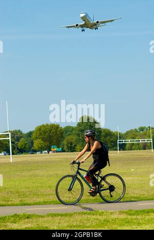 Arlington, Virginia, États-Unis - 11 septembre 2019 : une femme fait du vélo à Gravelly point, tandis qu'un avion régional approche l'aéroport national Ronald Reagan de Washington. Banque D'Images