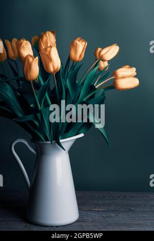 Tulipes dans une carafe. Classique encore vie avec un bouquet de fleurs de tulipe délicates dans un pot blanc vintage sur un fond vert et une vieille table en bois. Art Banque D'Images