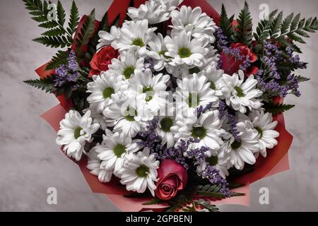 Un magnifique bouquet de chrysanthèmes blancs et de roses rouges sur un fond clair. Vue de dessus, gros plan. Banque D'Images