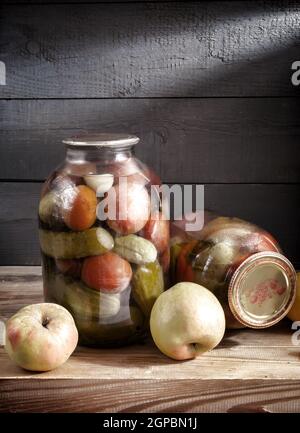 Sur une étagère dans le sous-sol se trouvent deux bocaux en verre avec des tomates en conserve, des concombres et des poivrons. Scellé avec un couvercle étanche. Vue de face, espace de copie. Banque D'Images