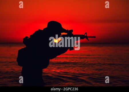 Silhouette de soldat de l'armée visant et tirant sur une carabine de service en se tenant debout au fond du genou dans l'eau de mer. Garde côtière, soldat des forces navales attaquant l'ennemi Banque D'Images