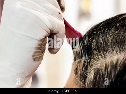 une jeune brune caucasienne mourant ses cheveux avec une brosse rose en utilisant des gants blancs à sa maison. Détails sur la brosse Banque D'Images