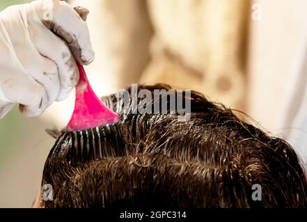 une jeune brune caucasienne mourant ses cheveux avec une brosse rose en utilisant des gants blancs à sa maison. Détails sur la brosse Banque D'Images