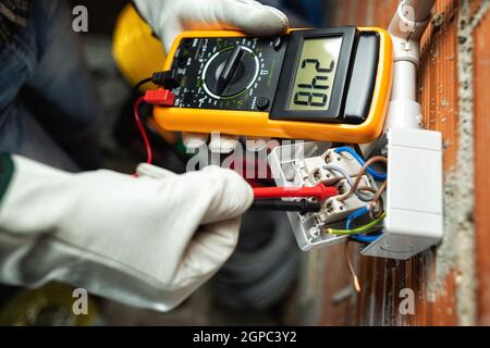Vue de dessus. Un électricien travaillant avec le testeur mesure la tension dans un commutateur d'un système électrique résidentiel. Travailler en toute sécurité avec p Banque D'Images