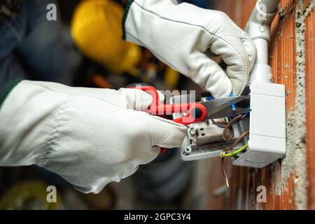 Vue de dessus. Un électricien au travail avec des ciseaux prépare les câbles électriques d'un système électrique résidentiel. Travailler en toute sécurité avec protectiv Banque D'Images