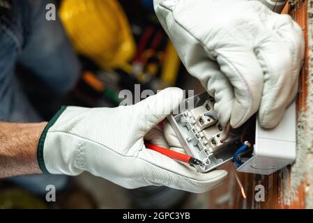 Vue de dessus. Un électricien au travail insère le câble électrique dans la pince d'un disjoncteur d'un système électrique résidentiel. Sécurité au travail Banque D'Images