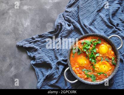 Shakshuka dans une casserole sur fond rustique gris. Plats traditionnels du Moyen-Orient. Œufs frits avec légumes. Espace pour le texte. Vue de dessus. Banque D'Images