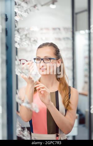 Femme étant satisfaite des nouvelles lunettes qu'elle a achetées dans le magasin les tenant devant son visage Banque D'Images