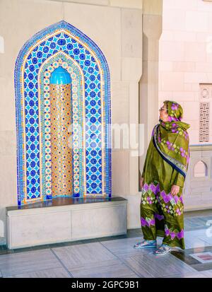 Une femme habillée dans une abaya omanaise traditionnelle qui regarde une alcôve ornée à la grande mosquée du Sultan Qaboos à Muscat, Oman Banque D'Images