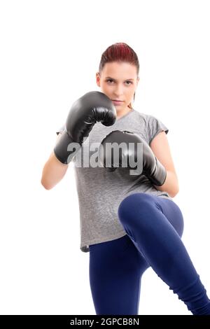 Portrait d'une belle jeune fille sérieuse avec des gants de boxe soulevant son genou, isolée sur fond blanc. Concept de sport de combat. Banque D'Images