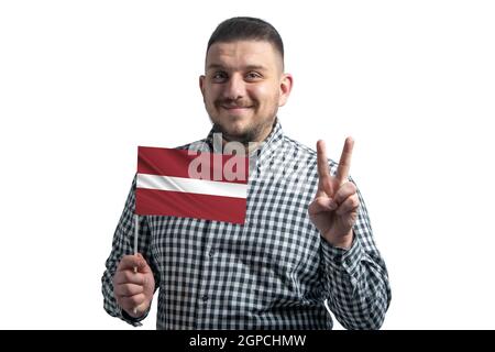Homme blanc tenant un drapeau de la Lettonie et montre deux doigts isolés sur un fond blanc. Banque D'Images