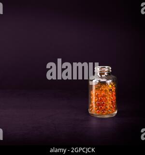 Un pot en verre avec des pilules de couleur jaune orange vif sur fond lilas. Placez l'étiquette, le logo, la mise en page. Banque D'Images