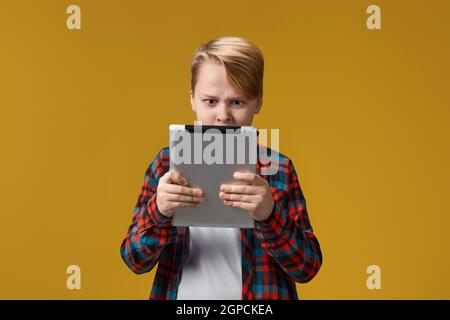 enfant en colère dans une chemise à carreaux avec une tablette numérique arrière-plan jaune Banque D'Images