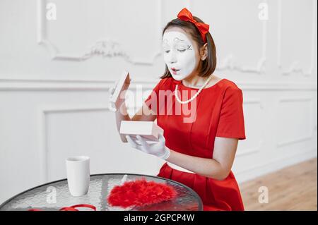 Artiste mime féminine en costume rouge, scène avec cadeau. Théâtre pantomime, comédien parody, émotion positive, performance d'humour, drôle de visage et gri Banque D'Images