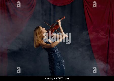 Violoniste féminine avec arc et violon, performance solo sur scène. Femme avec instrument de musique à cordes, art de la musique, musicien joue sur alto, backgro sombre Banque D'Images