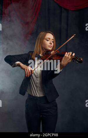 Violoniste féminine avec arc et violon, performance sur scène. Femme avec instrument de musique à cordes, art de la musique, musicien joue sur alto, fond sombre Banque D'Images