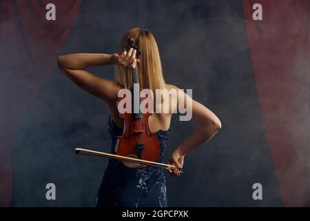 Violoniste féminine avec arc et violon derrière son dos, performance virtuose sur scène. Femme avec instrument de musique à cordes, art de la musique, musicien jouer sur Banque D'Images