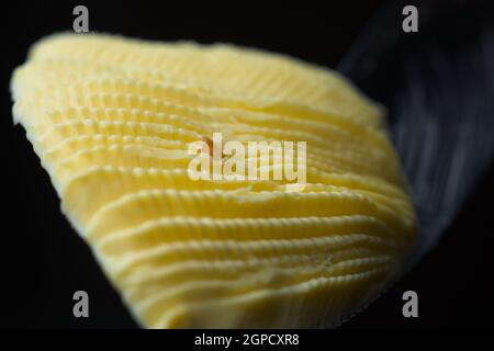 Le couteau dentelé maintient une boucle de margarine jaune ondulée en forme de ventilateur. Isolé sur fond noir et perspective super macro. Centrer également le fil à pain Banque D'Images