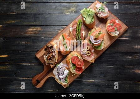 Brushetta ou des tapas espagnoles traditionnelles. Hors-d'antipasti italiens avec des collations. Variété de petits sandwichs au jambon, tomates cerises, du saumon Banque D'Images