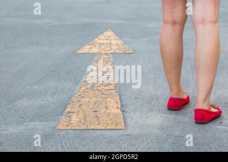 Fille porter des chaussures rouges marchant vers avec des panneaux de signalisation jaune sur un fond de route asphaltée Banque D'Images