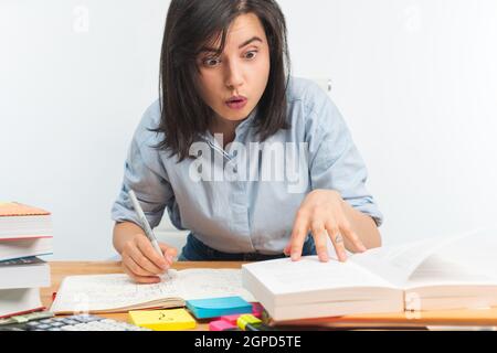 Vue de face d'une fille choquée qui étudie sur la table Banque D'Images