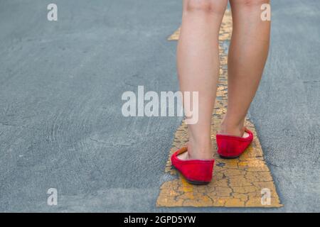 Fille porter des chaussures rouges marchant vers avec des panneaux de signalisation jaune sur un fond de route asphaltée Banque D'Images