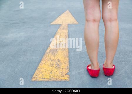 Fille porter des chaussures rouges marchant vers avec des panneaux de signalisation jaune sur un fond de route asphaltée Banque D'Images