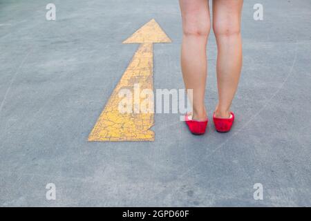 Fille porter des chaussures rouges marchant vers avec des panneaux de signalisation jaune sur un fond de route asphaltée Banque D'Images