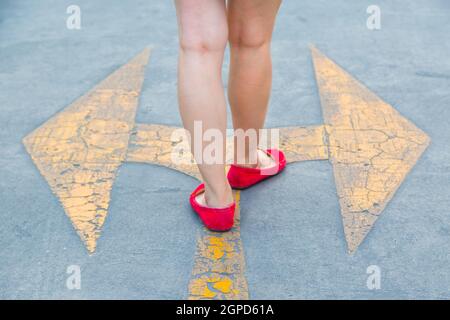 Fille porter des chaussures rouges marchant vers avec des panneaux de signalisation jaune sur un fond de route asphaltée Banque D'Images