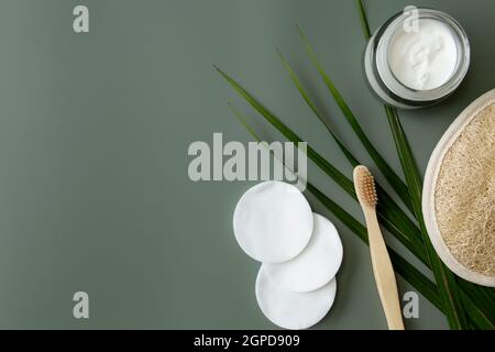 Accessoires de bain pose en toile de floy, fond vert pastel. Concept de soins de santé, feuille de palmier, brosse à dents en bois, crème, tampons de coton, débarbouillette. ECO, zéro déchet, Banque D'Images