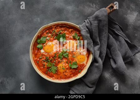 Shakshuka , petit-déjeuner traditionnel du Moyen-Orient - œufs frits, oignon, poivron, tomates et persil dans une casserole sur fond sombre Banque D'Images