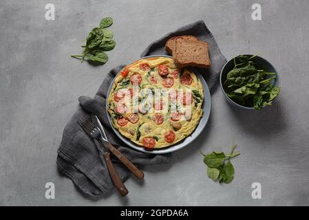 Frittata à base d'œufs, de champignons, de tomates cerises et d'épinards servis sur une assiette. Cuisine italienne. Banque D'Images