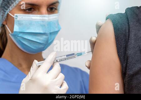 Infirmière en masque chirurgical vaccinant la personne contre les virus. Femme médecin en seringue de retenue respiratoire bleue à côté du bras. Femme dans les vêtements d'hôpital g Banque D'Images