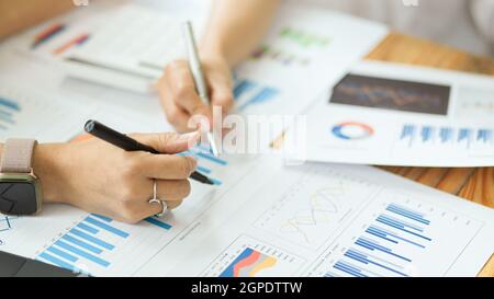 Focus mains image, deux de femme d'affaires analysant des graphiques et des graphiques financiers, prenant des notes sur le rapport financier Banque D'Images