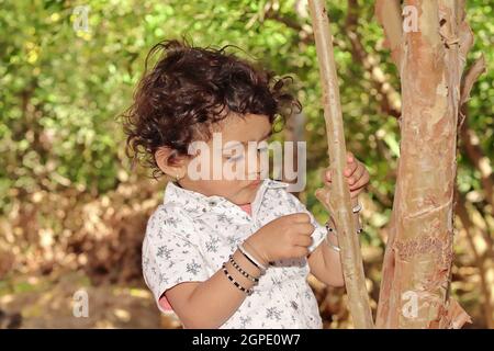 Gros plan d'Un petit enfant mignon d'une famille de fermiers hindous d'origine indienne regardant un ver sur un tronc d'arbre Banque D'Images