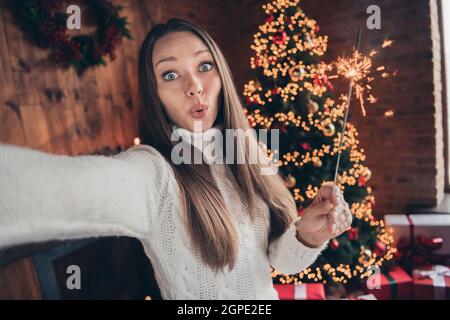 Photo de drôle impressionné jeune femme porter blanc Pullover tking selfie tenant des sparkles à l'intérieur maison maison chambre Banque D'Images