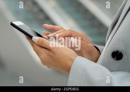 Mains de la jeune femme d'affaires en tenue grise touchant l'écran du smartphone Banque D'Images