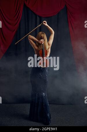 Violoniste féminine avec arc et violon derrière son dos, performance virtuose sur scène. Femme avec instrument de musique à cordes, art de la musique, musicien jouer sur Banque D'Images