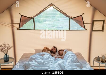 Jeune mari et femme dormant sur un grand lit double à l'intérieur d'une tente de glamping Banque D'Images