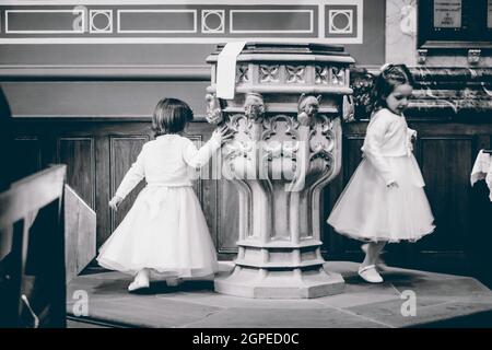 Une photo en niveaux de gris de petites filles caucasiennes miettes dans des robes blanches jouant au coin de la pièce Banque D'Images