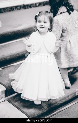 Une photo en niveaux de gris d'une petite fille de race blanche dans une robe blanche avec un visage souriant Banque D'Images