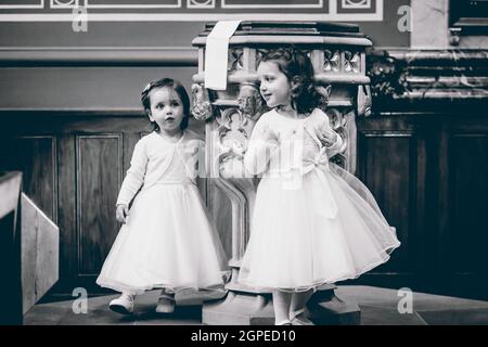 Une photo en niveaux de gris de petites filles caucasiennes miettes dans des robes blanches debout au coin de la pièce Banque D'Images