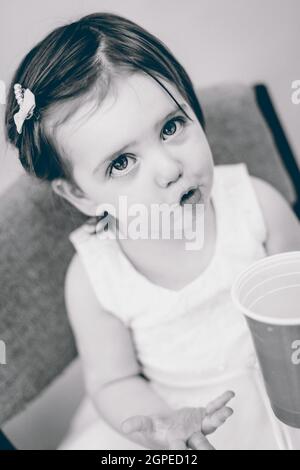 Une photo en niveaux de gris d'une petite fille caucasienne mignonne dans une robe blanche avec un visage surpris Banque D'Images